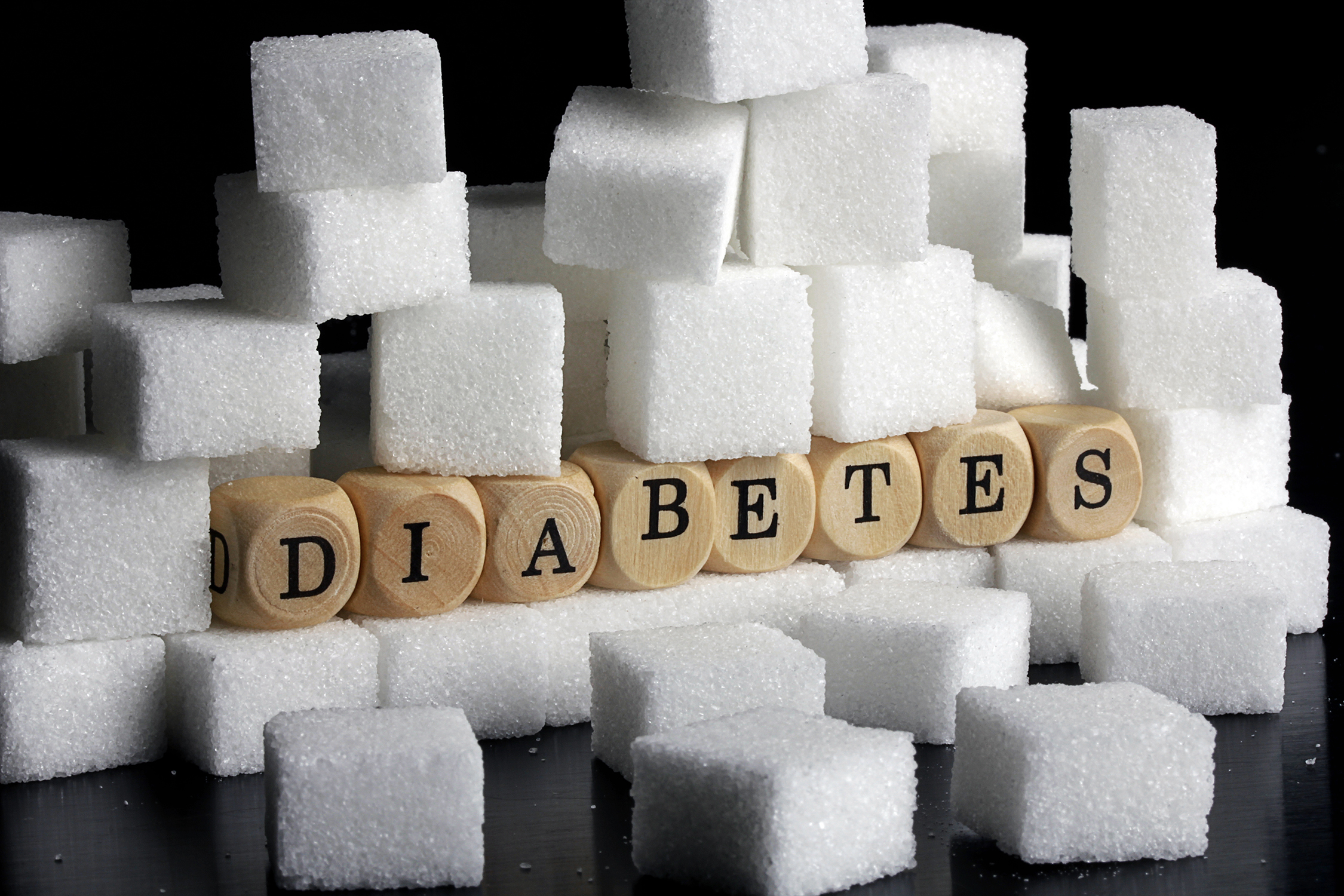 Das Foto ist ein Symbolbild für die Krankheit Diabetes, es zeigt den Begriff ausgeschrieben auf Holzwürfelchen in einem Berg von Zuckerwürfeln